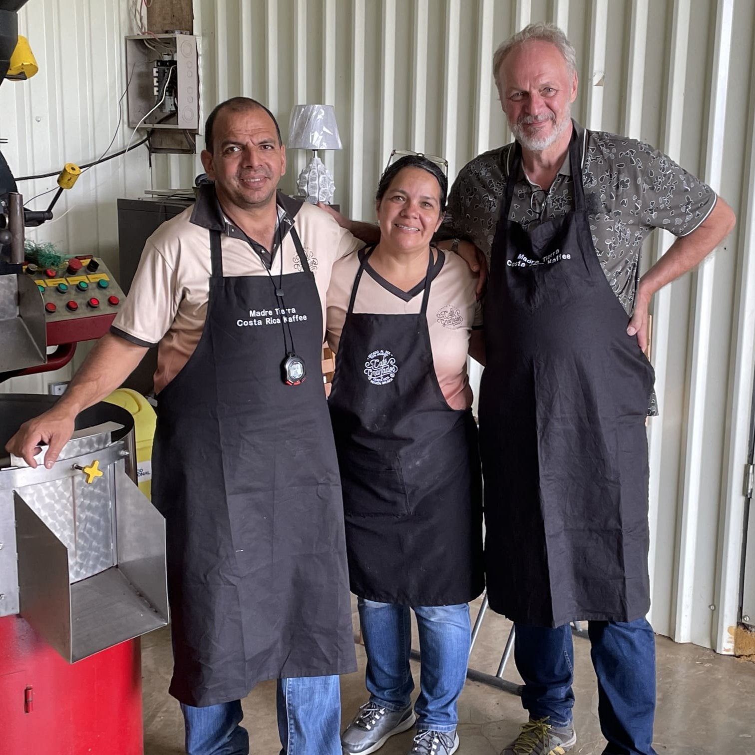 Pablo Sr, seine Frau und Wolfgang Neumann von Costa Rica Kaffee stehen vor einer Röstmaschine. Das Bild zeigt die Menschen hinter der nachhaltigen Kaffeeproduktion.