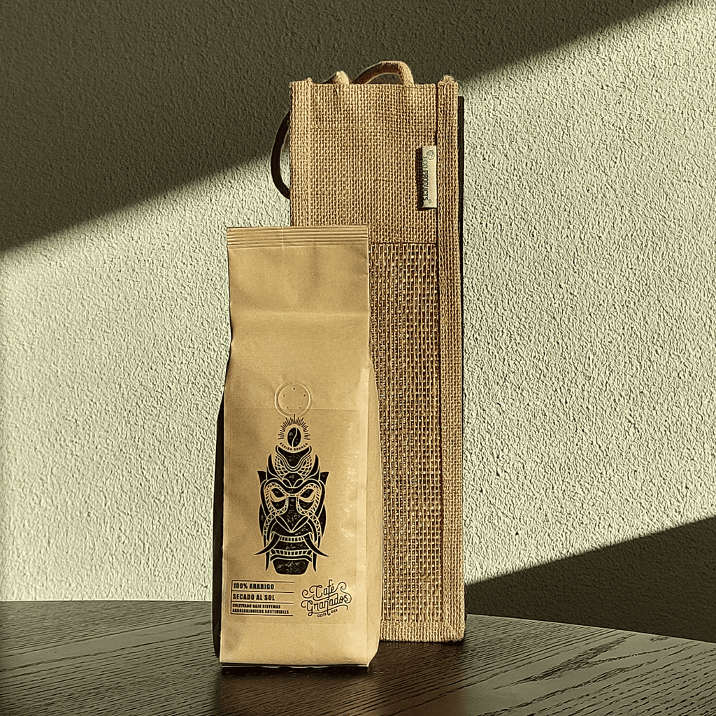 Kraftpapier-Kaffeepackung von Café Granados (Costa Rica Kaffee) vor einer Jutetasche auf einem Holztisch, im schrägen Sonnenlicht vor strukturierter Wand.