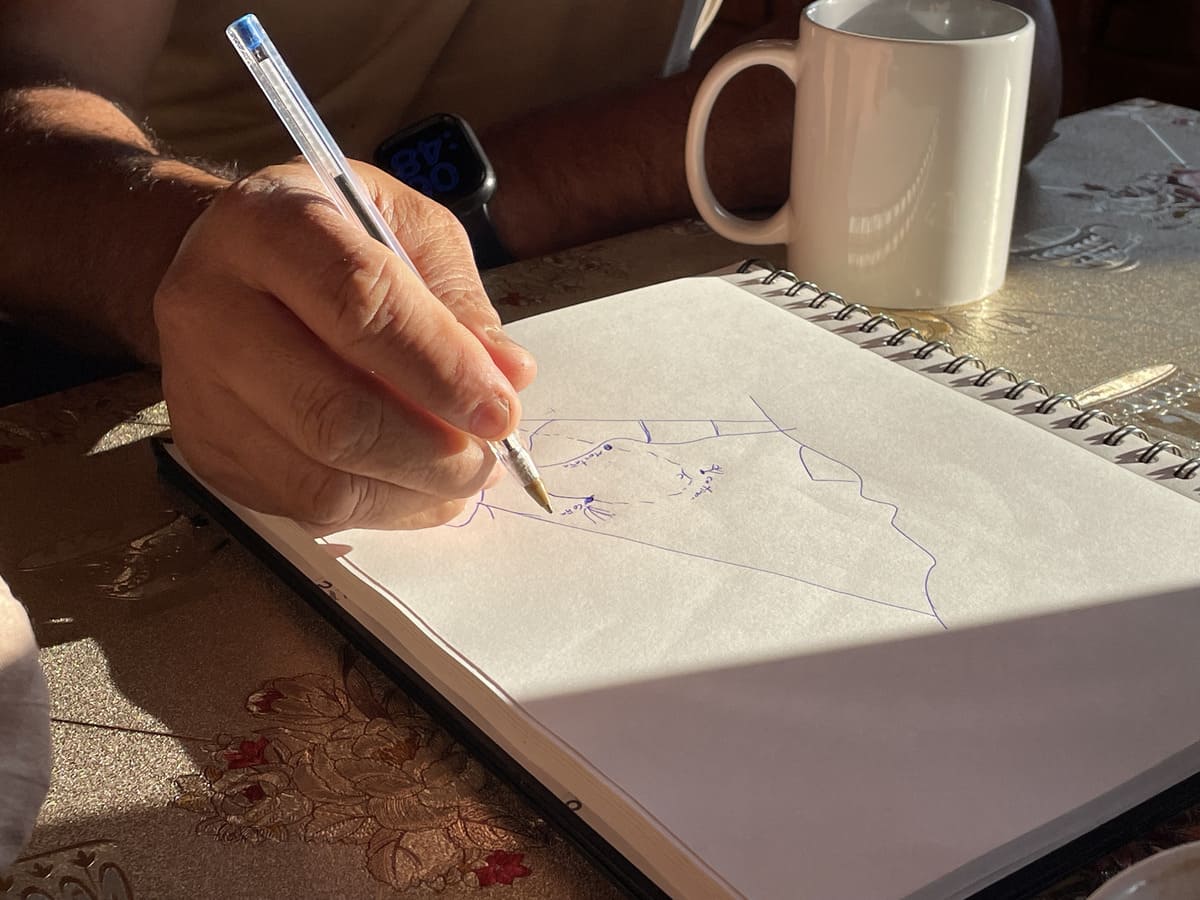 Nahaufnahme einer Hand, die auf der Farm Granados eine Skizze in ein Notizbuch zeichnet; daneben eine weiße Kaffeetasse – Costa Rica Kaffee.